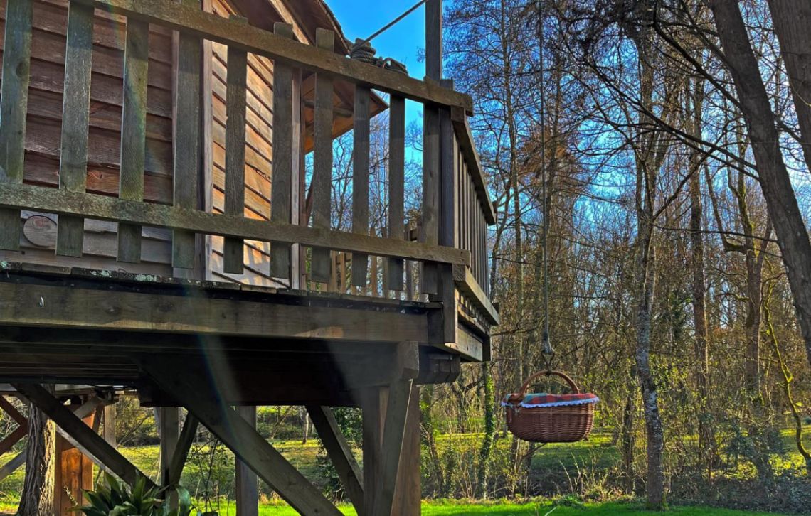 Un panier de petit déjeuner suspendu à une poulie devant la porte de la cabane Pêcheur de Lune, prêt à être hissé, illustrant le rite matinal authentique au Clos de Cyrano en Dordogne